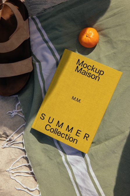 Yellow hardcover book on striped beach towel with fresh orange