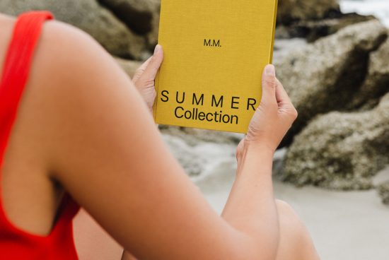Person holding a yellow book mockup with Summer Collection text, against a beach backdrop, ideal for designers to showcase cover designs.