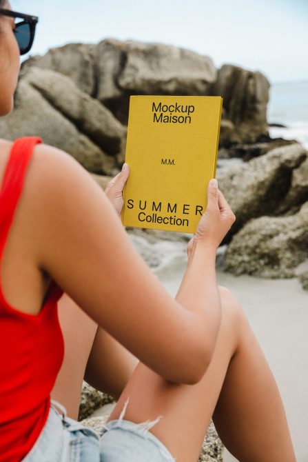 Woman on beach holding yellow book mockup with summer collection text, for graphic design and mockup resources.