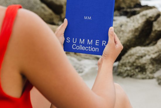 Person holding blue booklet with 'SUMMER Collection' text, mockup for design presentation, beach backdrop, close-up on item.