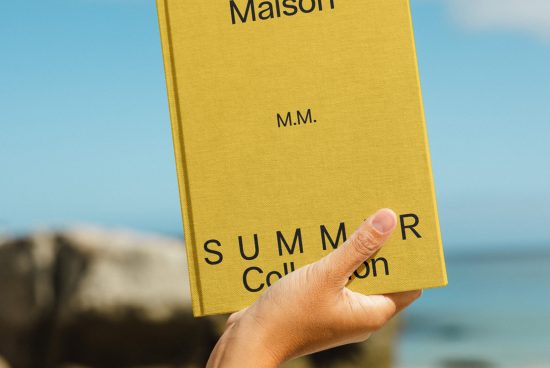 Hand holding a book mockup with yellow cover and black text against a blurred natural backdrop, ideal for design presentations.