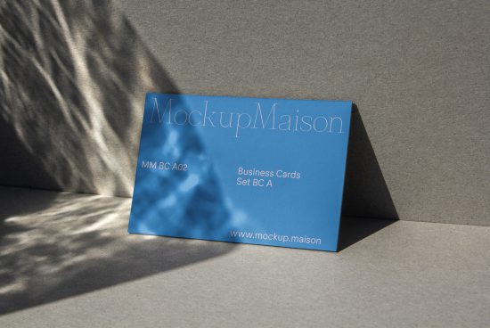 Blue business card mockup lying on textured surface with natural light and shadows, ideal for presentation and design projects.