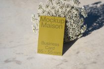 Gold business card mockup surrounded by white flowers on light sand