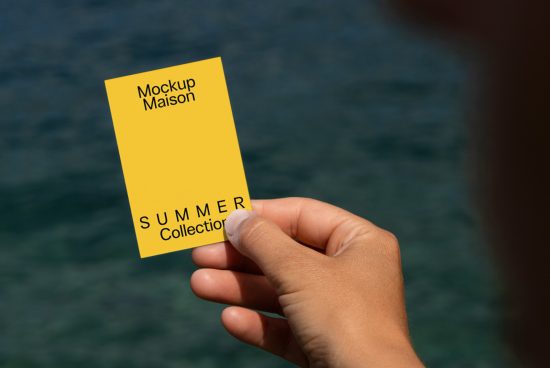 Hand holding a yellow card with mockup text by the sea, ideal for designers to showcase branding for summer collections.