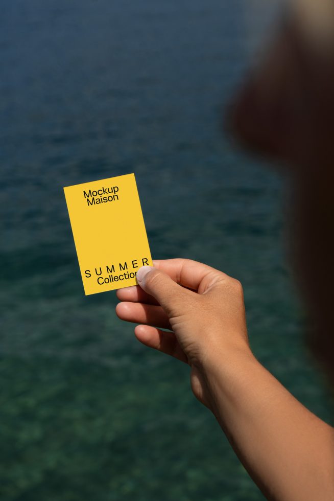 Person holding a yellow business card mockup with text for summer collection over water backdrop, ideal for designers and branding.