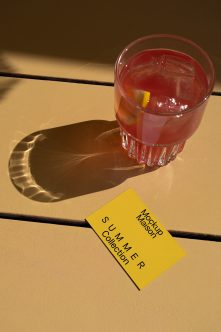 Yellow business card beside red drink with ice on warm tan wooden deck