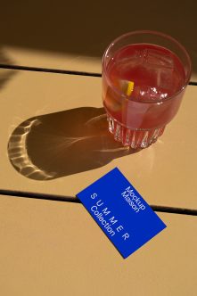 Blue business card next to cocktail glass with lemon twist on sandy surface