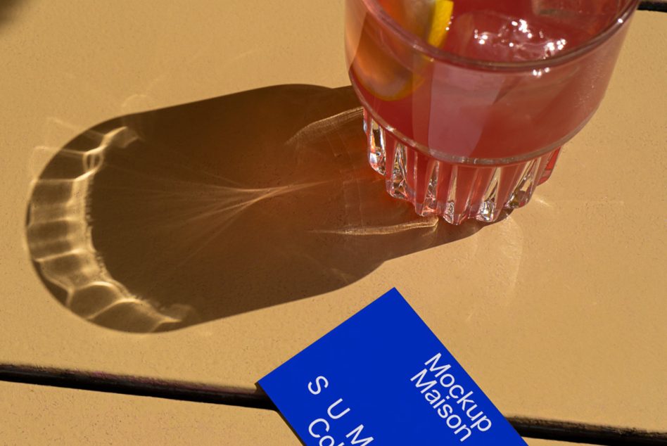 Blue card mockup positioned near tall glass of cranberry cocktail in sunlight