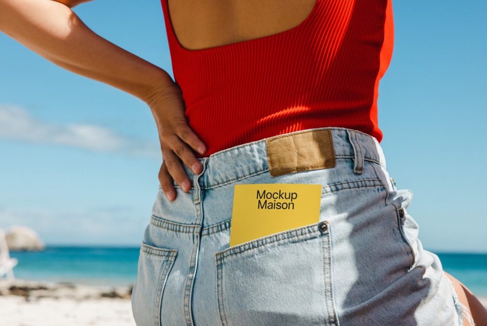 Yellow card mockup peeking from jeans pocket on beach with ocean background