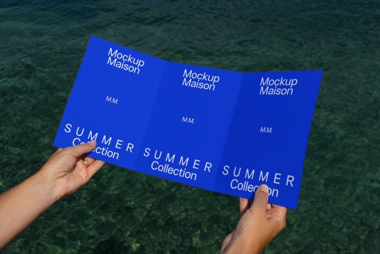 Hands holding three-fold brochure mockup with blue design for summer collection over water background, for graphic designers.