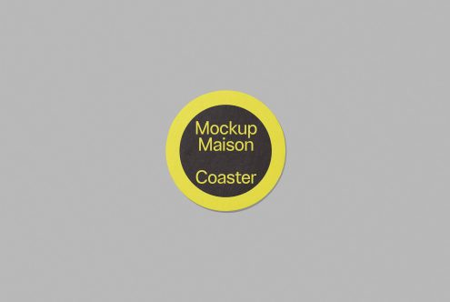 Round coaster mockup on a grey background with a yellow border and black center including the text Mockup Maison Coaster, perfect for graphic design presentations.