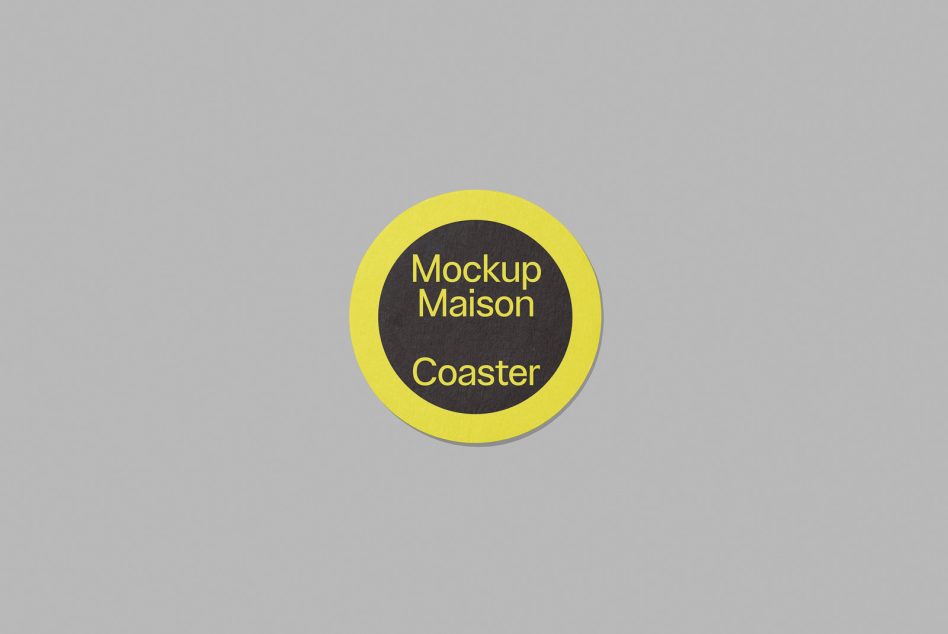 Round coaster mockup on a grey background with a yellow border and black center including the text Mockup Maison Coaster, perfect for graphic design presentations.