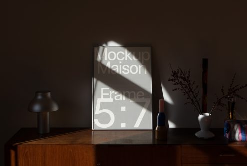 Elegant interior frame mockup on wooden cabinet with decorative vase and lamp, natural lighting, ideal for showcasing designs.