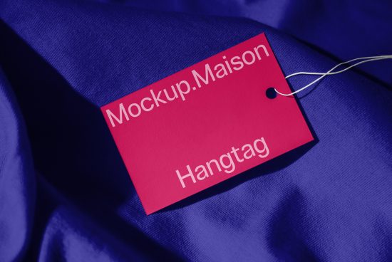 Pink hangtag mockup on blue fabric for product branding, realistic label design presentation, clothing tag template for designers.