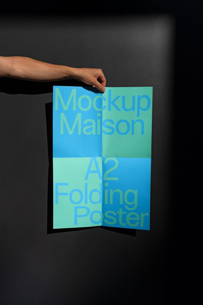 Hand holding an unfolded A2 size poster mockup against a dark wall, with typographic design, showcasing print presentation for graphic designers.