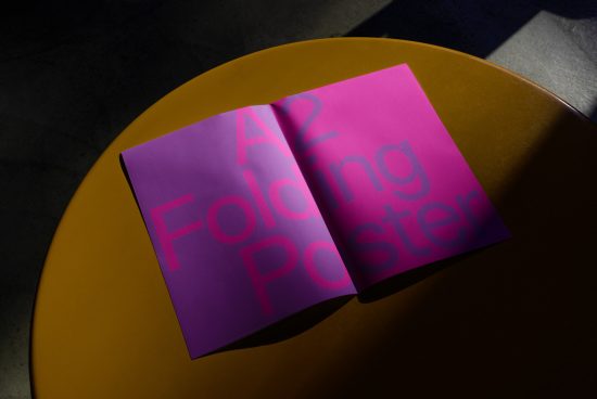 Open A2 folding poster mockup on yellow round table with dramatic lighting, showcasing typography and print design, ideal for portfolio presentation.