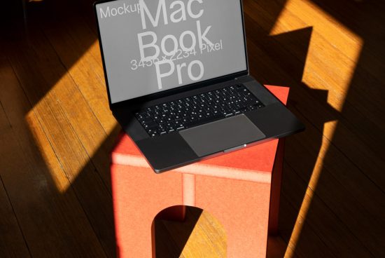 Laptop mockup on orange stool with sunlight casting shadows, ideal for digital asset showcasing in graphic design.