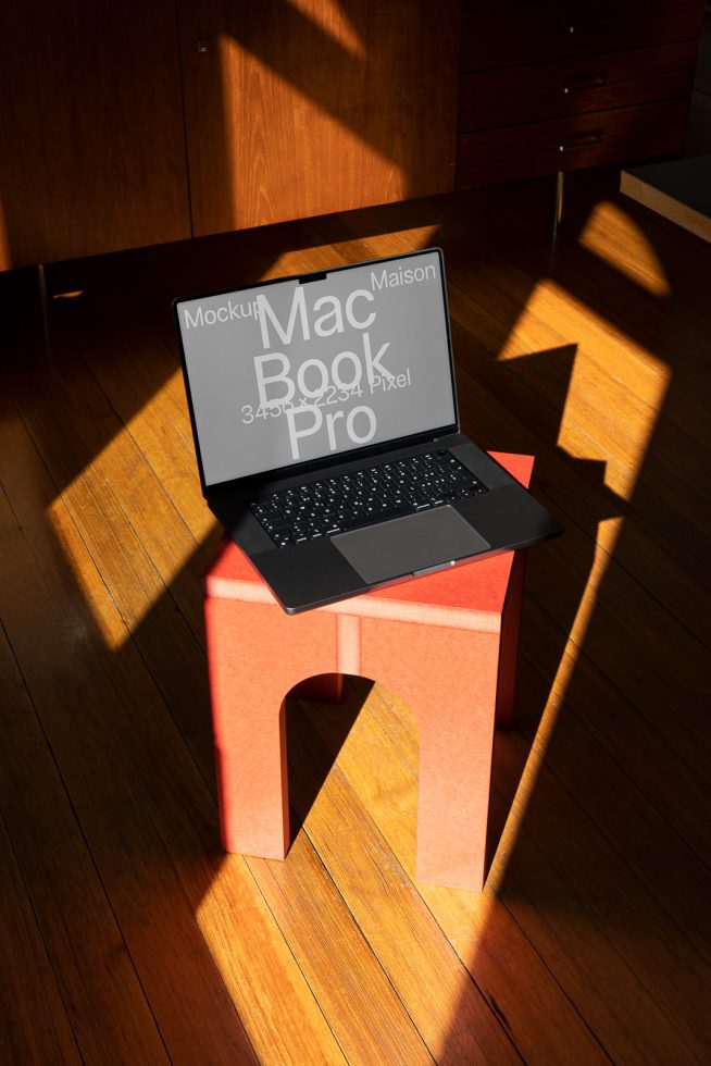 Laptop on orange stool with screen showing text Macbook Pro, ideal for mockup templates, digital design assets, realistic shadows, interior setting.