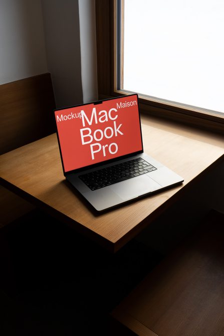 Laptop mockup on desk next to window, MacBook Pro screen with editable design, modern workspace, digital asset for designers.