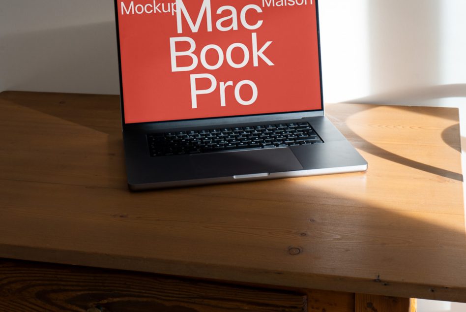 MacBook Pro on wooden desk with coral red screen mockup, low angle perspective