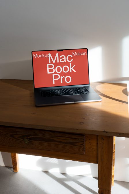MacBook Pro on wooden desk with coral red screen mockup, soft natural shadows