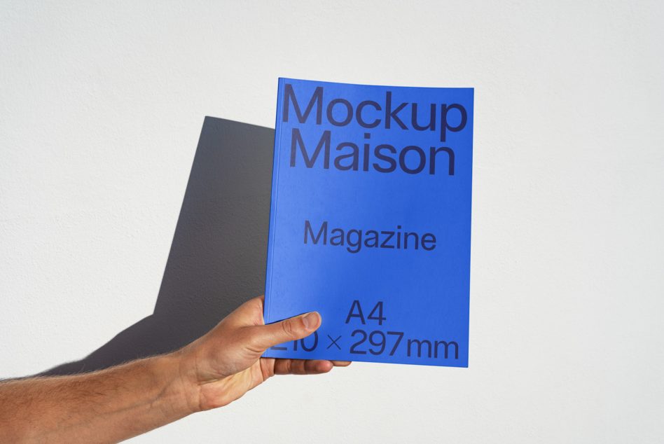 Hand holding a blue magazine mockup with clear typography against a white background, showcasing design presentation for A4 format.