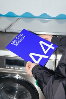 Hand holding blue A4 paper mockup above washing machine with wavy background