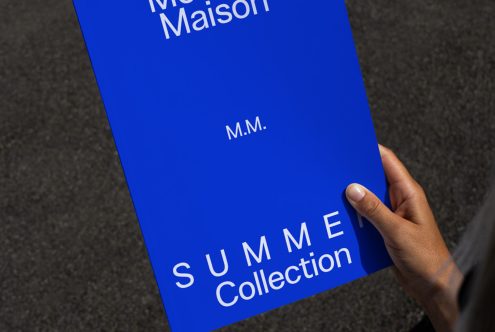 Person holding a blue fashion magazine mockup with white text, useful for presenting design layouts and font work.