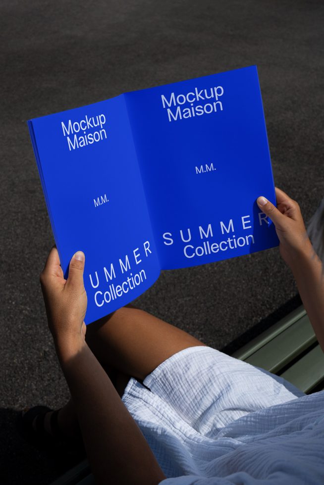 Person holding open magazine with blue cover mockup design showcasing 'Mockup Maison' brand, ideal for designers creating print templates.