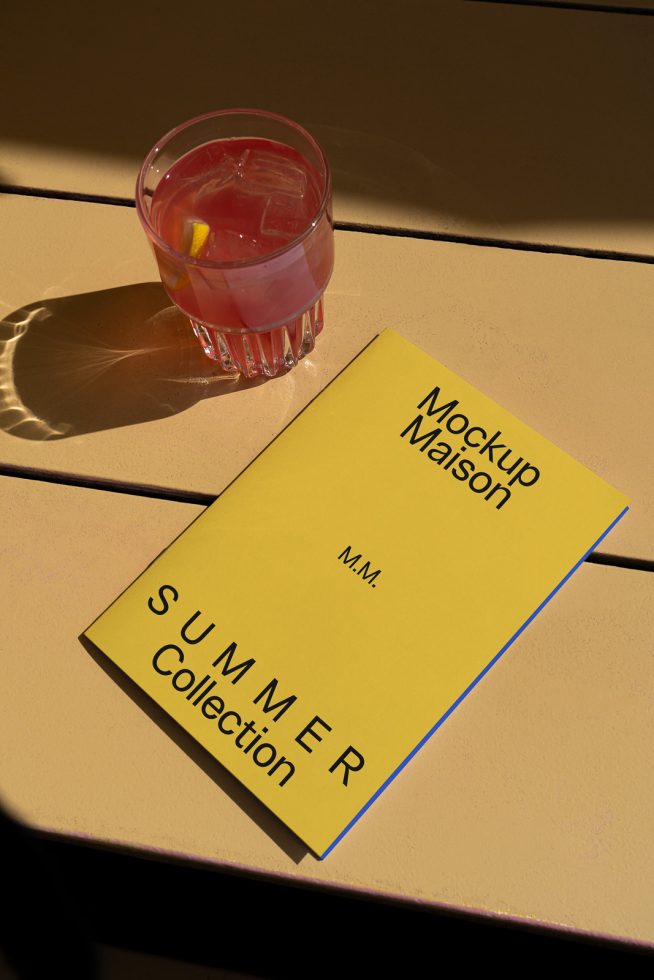 Yellow magazine mockup on a table with a refreshing drink casting a shadow, ideal for summer collection presentations for designers.