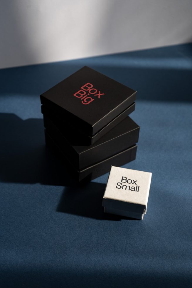 Stack of three black boxes with red text 'Box Big' next to a small white box with text 'Box Small' on a blue background, product mockup.