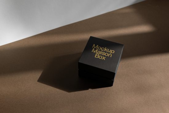 Black box packaging mockup with elegant gold lettering on a textured paper background, ideal for designers interested in product presentation.
