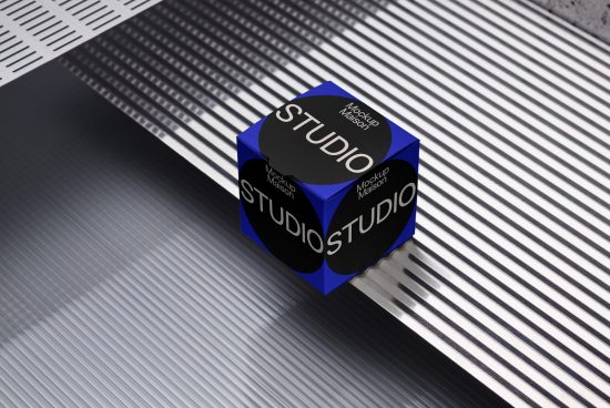 3D packaging mockup of a blue cube with the word STUDIO on a striped shadowed background, ideal for branding presentations.