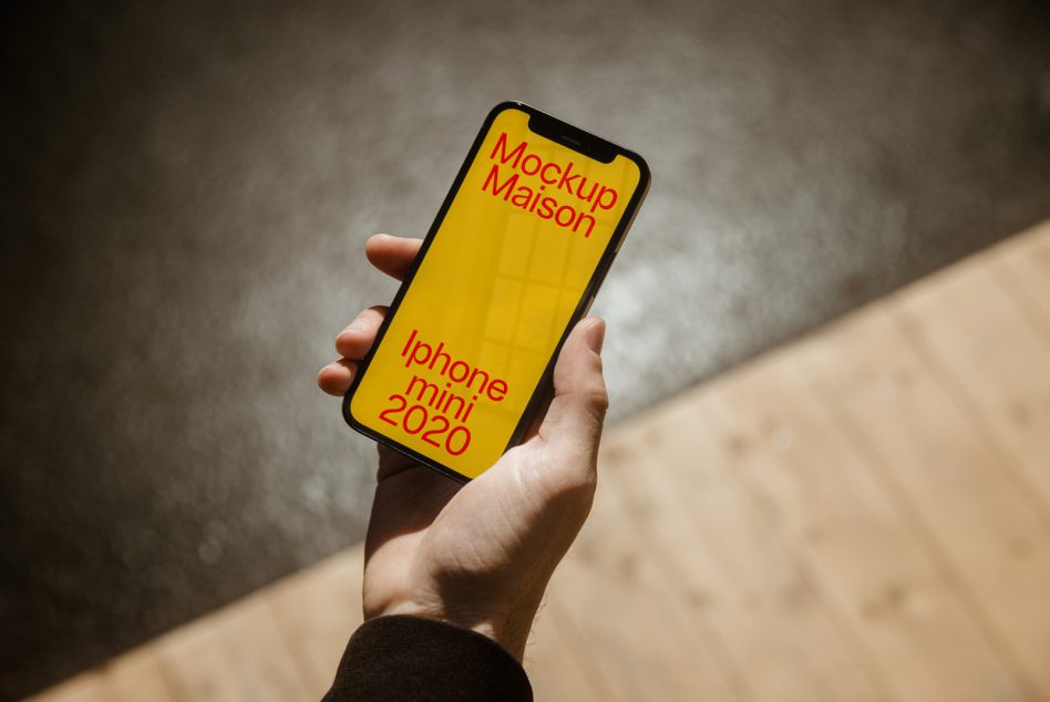 Hand holding smartphone with vibrant yellow screen mockup, text overlay 'Mockup Maison iPhone mini 2020', ideal for designers, digital assets.