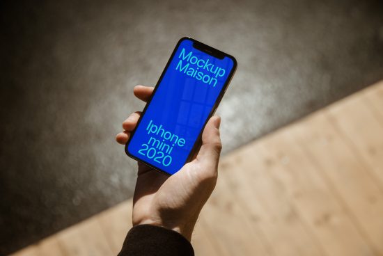 Hand holding smartphone mockup displaying blue screen with text, wooden floor background, for app design presentation.