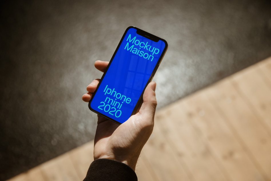 Hand holding smartphone mockup displaying blue screen with text, wooden floor background, for app design presentation.