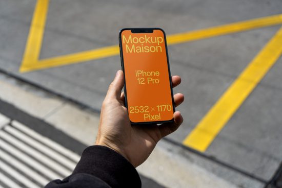 Hand holding iPhone 12 Pro with screen mockup on urban background, ideal for showcasing mobile app designs.