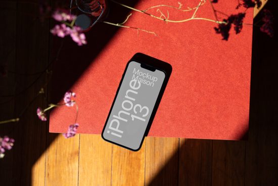 Stylish iPhone 13 mockup on a red surface with natural lighting and floral shadow overlay, ideal for showcasing app designs.