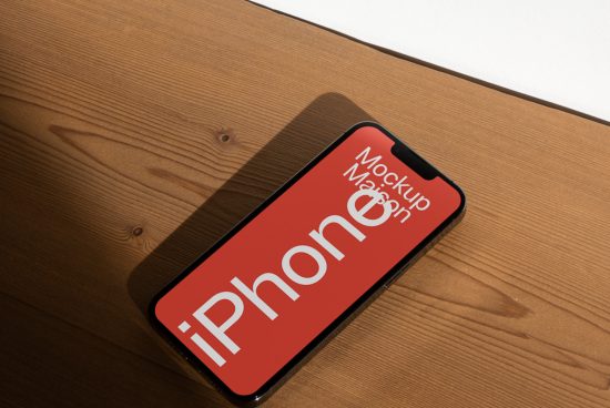 Smartphone on wooden surface displaying red screen with mockup text, ideal for showcasing app UI designs.