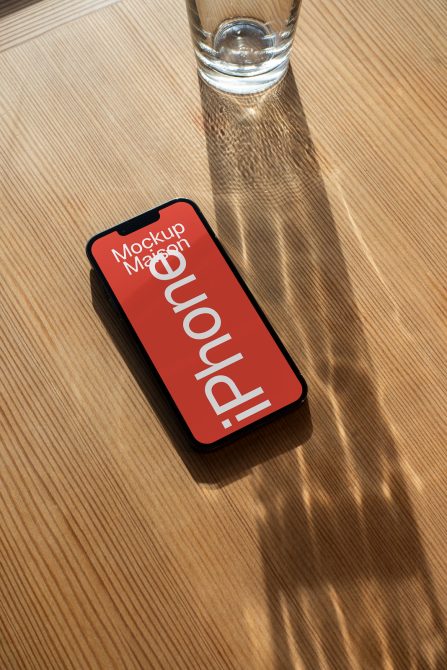 Red iPhone mockup on light wood table with water glass casting shadow above