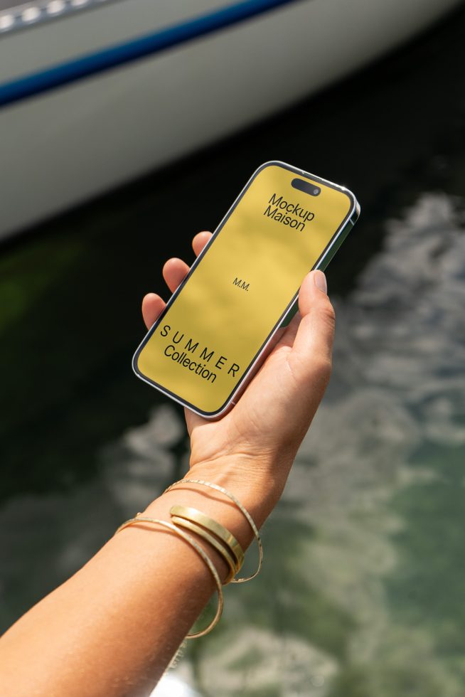 Hand holding smartphone with summer collection screen mockup near water, ideal for showcasing mobile designs for designers.