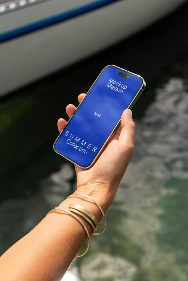 Person holding smartphone with blue screen mockup, outdoor setting with water backdrop, digital asset for graphic designers.