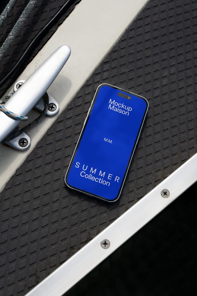 Smartphone mockup on a yacht deck displaying blue screen with text Mockup Maison Summer Collection, ideal for showcasing design apps and themes.