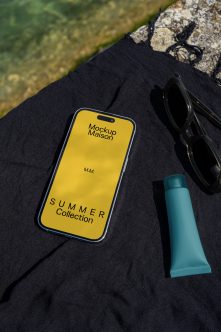 Yellow phone mockup on black fabric styled with sunglasses plus teal beauty tube