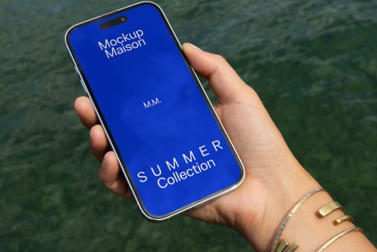 Hand holding smartphone mockup with blue screen displaying text Mockup Maison Summer Collection against water background.