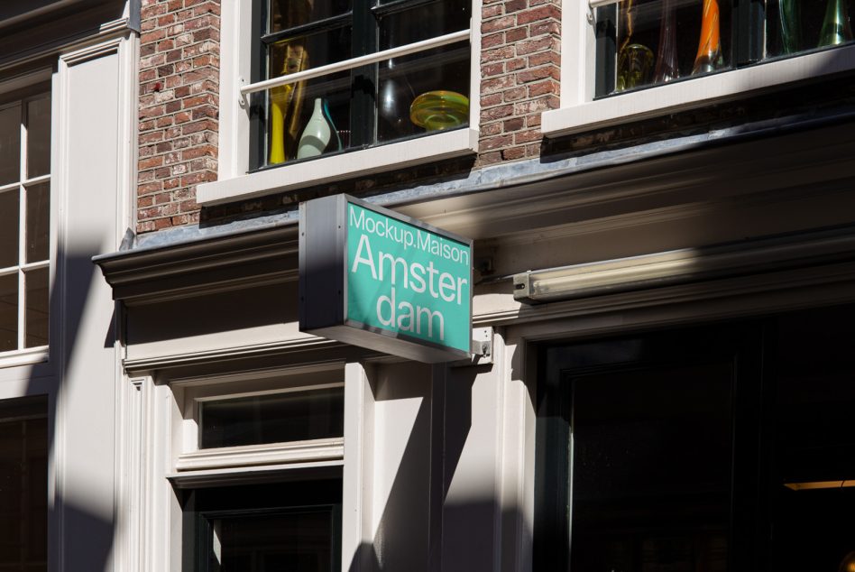 Teal glowing Amsterdam sign protruding from historic storefront with brick above