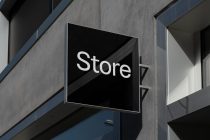Square black storefront sign with white sans-serif text on modern concrete building facade
