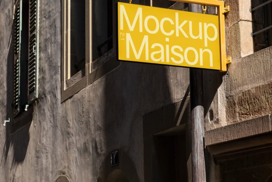 Yellow signboard with Mockup Maison text hanging on a sunlit urban building wall, ideal for designers seeking realistic mockup graphics.