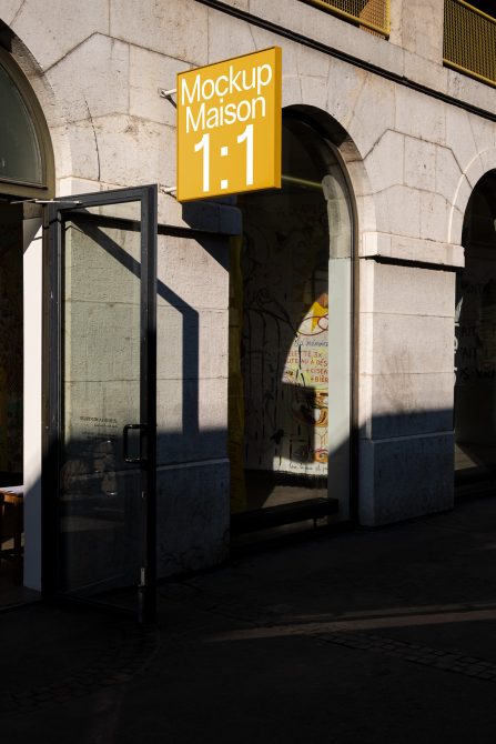 Golden yellow square sign on gold frame above black storefront glass door, daytime