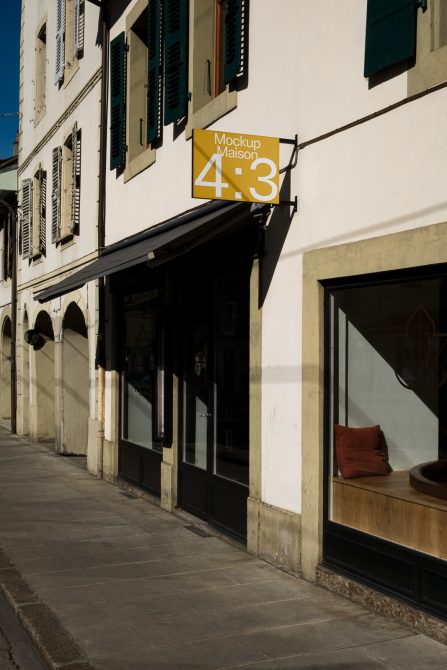 Storefront signage mockup displayed on an urban shop facade with clear skies and shadows, ideal for designers creating mockups.